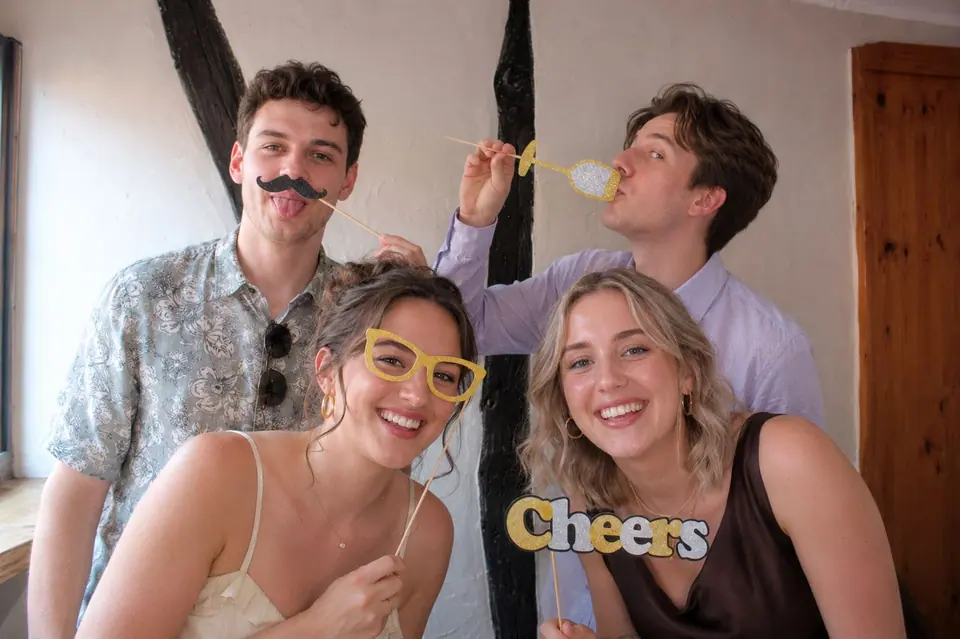 Vier Freunde mit Schnurrbart-, Brillen- und „Cheers“-Requisiten